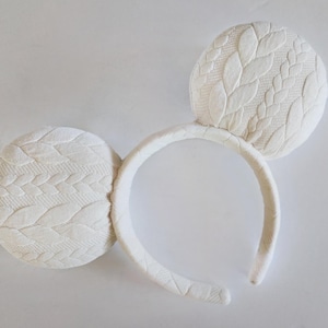 May include: White headband with two white knit fabric ears. The ears have a cable knit pattern.