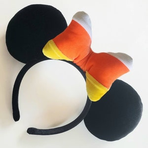 May include: Black mouse ears headband with a large orange, yellow, and white candy corn bow.