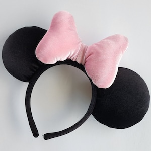 May include: Black headband with two large black ears and a pink velvet bow. The headband is designed to look like Mickey Mouse ears.