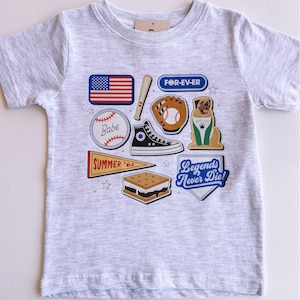 May include: Gray short-sleeved t-shirt with a variety of colorful patches, including a baseball, a baseball glove, a s'more, a sneaker, a dog, a baseball bat, an American flag, a pennant that says "Summer '62", and a patch that says "Legends Never Die!" and "For-Ev-Er".