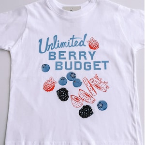 May include: White t-shirt with the text "Unlimited Berry Budget" in blue script. The shirt features illustrations of blueberries, raspberries, blackberries, and sliced strawberries in red and black.