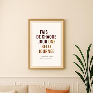 Può includere: Una stampa incorniciata con il testo francese "FAIS DE CHAQUE JOUR UNE BELLE JOURNÉE" in bordeaux e marrone. La stampa è appesa sopra un divano beige con cuscini arancioni e crema. Una pianta in vaso è a destra.