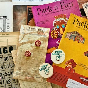 May include: A collection of vintage ephemera, including two "Pack-o-Fun" magazines, a bingo card, a guest check, and round "Strong!" drink tokens. The magazines are yellow and purple, with colorful illustrations. The bingo card has red number markers.