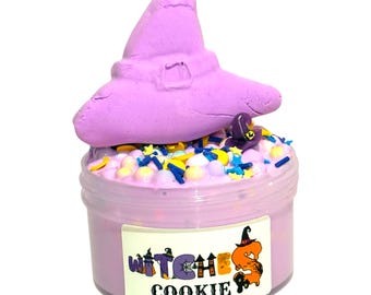 Könnte beinhalten: Ein Glas lavendelfarbener Schleim, gekrönt von einem großen, hellvioletten Hexenhut und bunten Streuseln. Ein kleinerer Hexenhut sitzt auf dem Schleim. Das Glas hat ein Etikett mit der Aufschrift "Witches Cookie" mit einer Cartoon-Hexe.