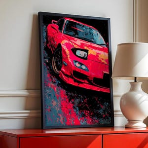 May include: A framed art print depicting a red sports car. The artwork uses an abstract style with red, black, and blue splashes. The print is displayed on a red cabinet, beside a white lamp with a cream lampshade.