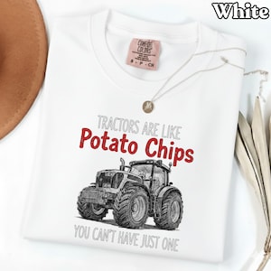 Puede incluir: Camiseta blanca con un gráfico de tractor y el texto "Tractors are like Potato Chips, You can't have just one." La camiseta tiene una etiqueta Comfort Colors y un collar plateado con un colgante.