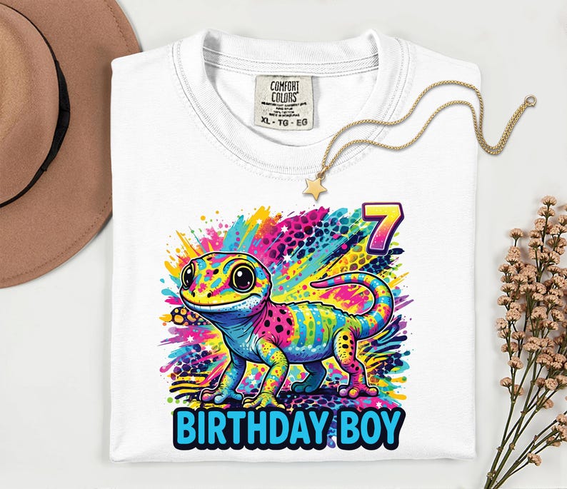 White t-shirt with a colorful gecko graphic. The gecko is depicted with vibrant hues of pink, blue, yellow, and green. The number 7 and the words "BIRTHDAY BOY" are also featured on the shirt.