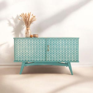 May include: A teal blue cabinet with two doors and a geometric pattern. The cabinet has a white background with a teal blue geometric pattern. The cabinet is sitting on a white floor.