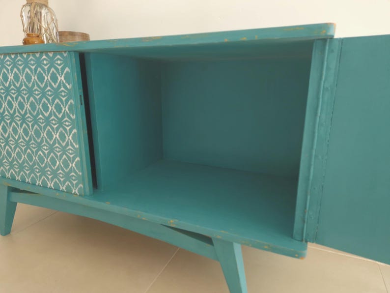 May include: Teal blue cabinet with a single door and a patterned panel on the other side. The cabinet has a simple design with angled legs.