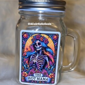Pode incluir: Um frasco de vidro transparente com tampa e alça prateadas. O frasco apresenta um autocolante colorido com um esqueleto usando uma coroa de flores e o texto "THE HOT MAMA". O autocolante tem uma borda floral.