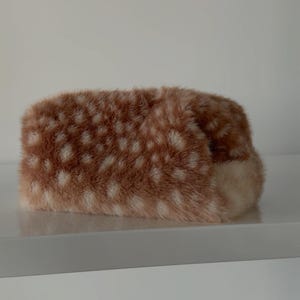 May include: A rectangular tissue box cover featuring a soft, faux fur texture with a brown and white spotted pattern resembling a fawn's coat. The cover has a plush, fuzzy appearance with a consistent pattern of white spots on a brown base.