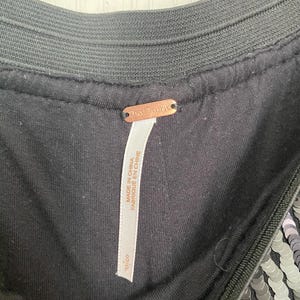 Op de afbeelding: Close-up van een zwart kledingstuk met een paillettenontwerp. Het kledingstuk heeft een zwarte elastische tailleband en een label met de tekst "Free People" en "Made in China / Fabriqu&eacute; en Chine". Het label geeft ook maat "S/P" aan.