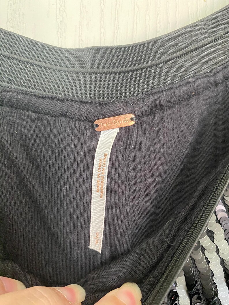Op de afbeelding: Close-up van een zwart kledingstuk met een paillettenontwerp. Het kledingstuk heeft een zwarte elastische tailleband en een label met de tekst "Free People" en "Made in China / Fabriqu&eacute; en Chine". Het label geeft ook maat "S/P" aan.
