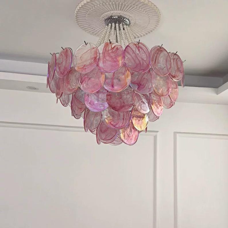May include: A decorative chandelier featuring a cascade of pink, translucent, shell-shaped elements. The light fixture is suspended from a silver-toned canopy with beaded strands, and is mounted on a white ceiling.