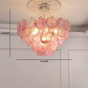 May include: A pink and clear chandelier with a diameter of 24 inches and a height of 24 inches. The light fixture has a circular design with multiple layers of pink, petal-shaped elements. The fixture is suspended from the ceiling.