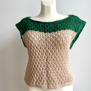 Puede incluir: Top de ganchillo hecho a mano, de dos tonos. El top presenta un escote y mangas cortas de color verde oscuro, con un cuerpo beige de tejido abierto. La prenda se exhibe en un maniqu&iacute;, mostrando su textura y dise&ntilde;o. Este top es una adici&oacute;n elegante a cualquier guardarropa.