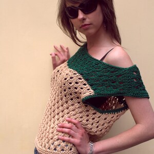 Puede incluir: Top de ganchillo beige y verde con dise&ntilde;o asim&eacute;trico. El top presenta un patr&oacute;n de tejido abierto y se combina con pantalones cortos de mezclilla. La persona lleva gafas de sol negras.