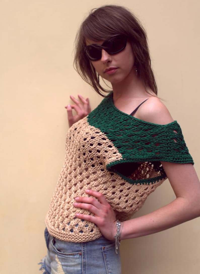 Puede incluir: Top de ganchillo beige y verde con dise&ntilde;o asim&eacute;trico. El top presenta un patr&oacute;n de tejido abierto y se combina con pantalones cortos de mezclilla. La persona lleva gafas de sol negras.