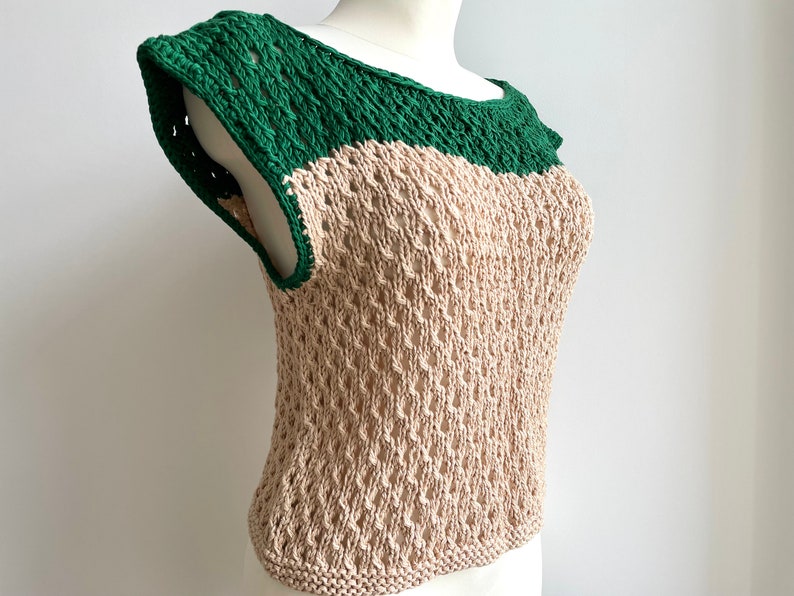 Puede incluir: Una blusa sin mangas de dos tonos con un dise&ntilde;o de tejido abierto. El cuello y los hombros son verdes, mientras que el cuerpo es beige. La tela de punto tiene un patr&oacute;n texturizado y abierto. La blusa se muestra en un maniqu&iacute;.