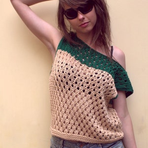 Puede incluir: Top de ganchillo beige y verde con dise&ntilde;o asim&eacute;trico. El top presenta un patr&oacute;n texturizado de tejido abierto y se combina con pantalones cortos de mezclilla. La persona lleva gafas de sol.