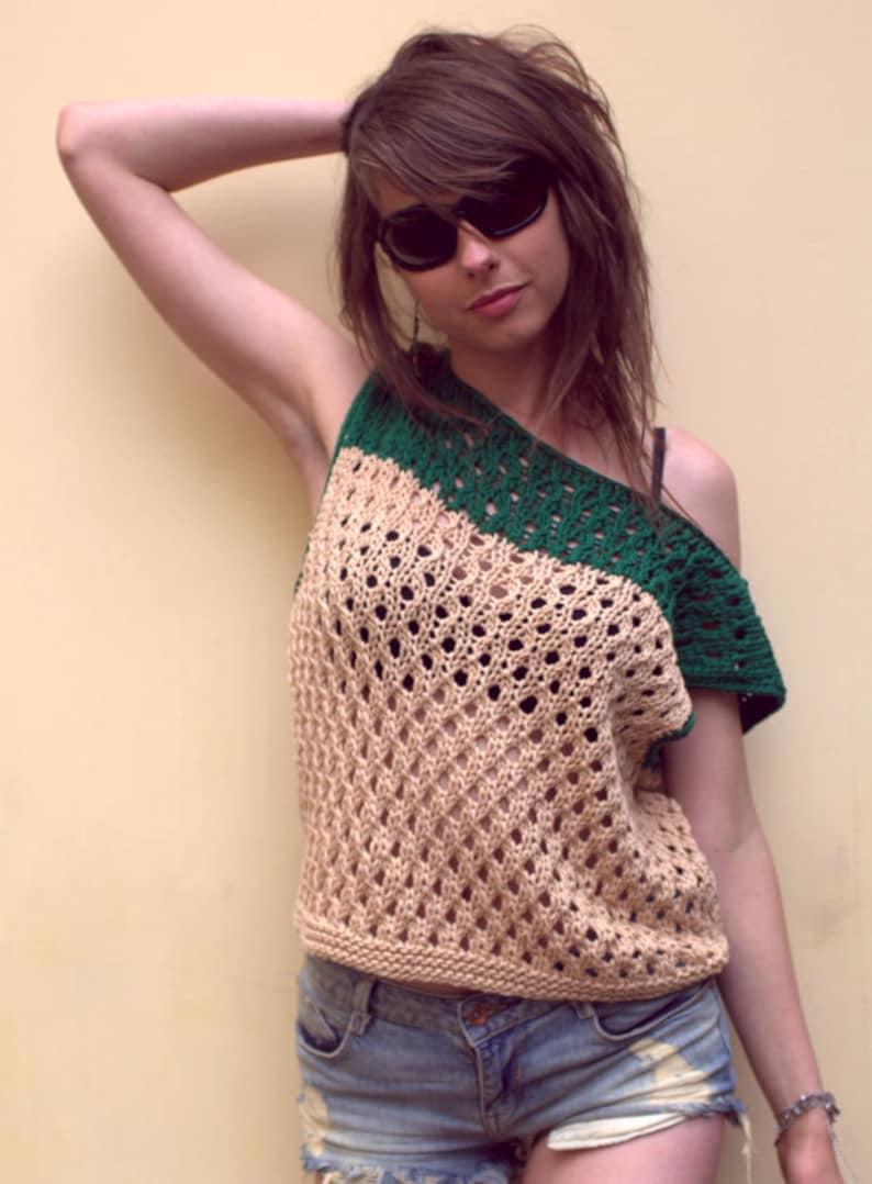 Puede incluir: Top de ganchillo beige y verde con dise&ntilde;o asim&eacute;trico. El top presenta un patr&oacute;n texturizado de tejido abierto y se combina con pantalones cortos de mezclilla. La persona lleva gafas de sol.