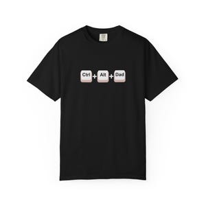 May include: Black t-shirt with the text "Ctrl + Alt + Dad" in a keyboard key design. The graphic is centered on the front of the shirt. The shirt has short sleeves and a crew neck.