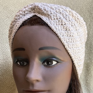 May include: A light gray crocheted turban headband. The headband is made with a simple stitch pattern and has a knotted detail on top.