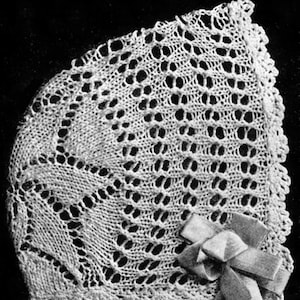 May include: A white crocheted baby bonnet with a delicate lace pattern. The bonnet has a bow tied on the side.
