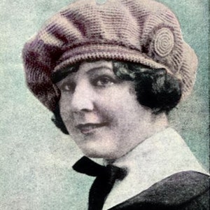 Puede incluir: Una mujer con un gorro de punto de ganchillo con un botón grande y decorativo en el lateral. El gorro es de color rosa claro y la mujer tiene el pelo oscuro.