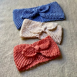 May include: Three crocheted headbands in different colors: blue, cream, and coral. Each headband has a knotted bow in the center.