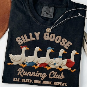 May include: Black t-shirt with the text "SILLY GOOSE Running Club" and a graphic of five geese in running attire. The shirt also has the text "EAT. SLEEP. RUN. HONK. REPEAT."