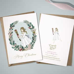 A Christmas card featuring a watercolour illustration of Clara in a white dress holding a nutcracker. The illustration is surrounded by a wreath of holly, berries, and other festive greenery. The card reads "Merry Christmas".