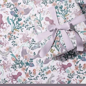 May include: A pink and purple mermaid wrapping paper with a repeating pattern of mermaids, sea creatures, and flowers. The text "Mermaid Wrapping Paper" and "www.cassandra riley designs.com" is printed at the bottom of the paper.