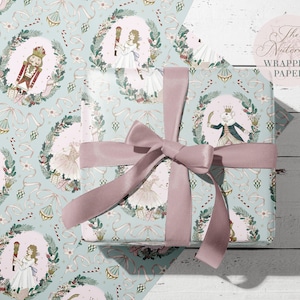 May include: A light blue wrapping paper with a repeating pattern of a Nutcracker, a ballerina, and a wreath of holly and berries. The text "The Nutcracker Wrapping Paper" is printed in the top right corner.