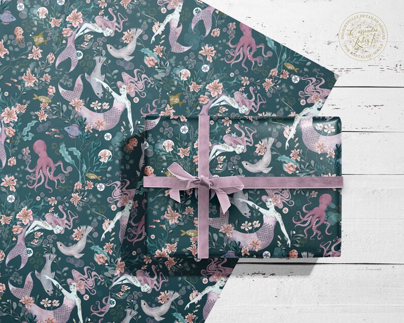 A sheet of teal blue wrapping paper with a repeating pattern of mermaids, octopuses, seashells, and flowers. The paper is wrapped around a gift box with a purple ribbon.