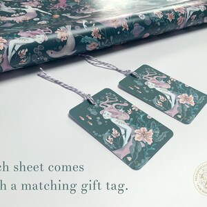 May include: Two teal gift tags with a mermaid illustration and pink flowers. The text on the tag reads "Delightfully Detailed Designs Caffanidis Play for Nostalgic Souls".