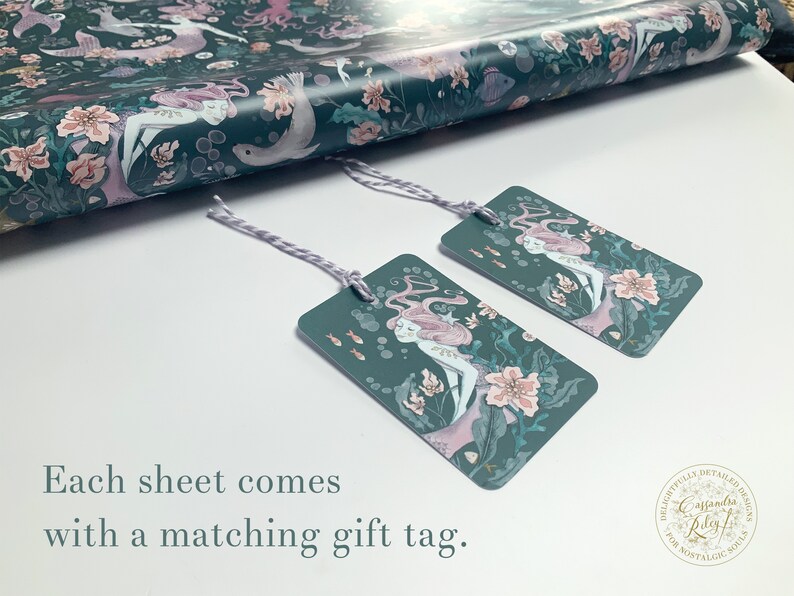 May include: Two teal gift tags with a mermaid illustration and pink flowers. The text on the tag reads "Delightfully Detailed Designs Caffanidis Play for Nostalgic Souls".