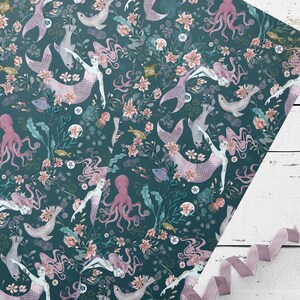 Teal blue wrapping paper with a repeating pattern of pink mermaids, pink octopuses, and sea creatures. The pattern is surrounded by a floral design in shades of pink and white.