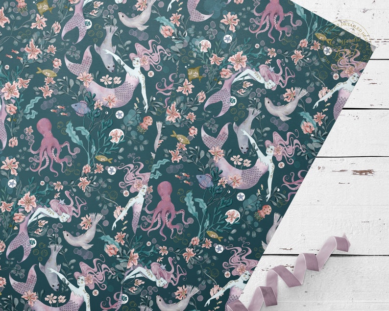 Teal blue wrapping paper with a repeating pattern of pink mermaids, pink octopuses, and sea creatures. The pattern is surrounded by a floral design in shades of pink and white.