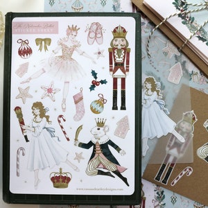 May include: A sheet of stickers featuring characters from The Nutcracker Ballet. The stickers include a ballerina, a nutcracker, a mouse king, and other festive elements. The stickers are printed on white paper with a glossy finish.