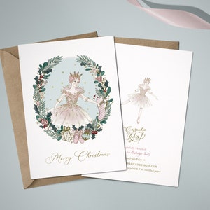 A Christmas card featuring the Sugar Plum Fairy in a pink tutu and a crown, surrounded by a wreath of holly, berries, and ornaments. The text "Merry Christmas" is printed below the ballerina. The back of the card features a smaller image of the ballerina and the artist's name and website.