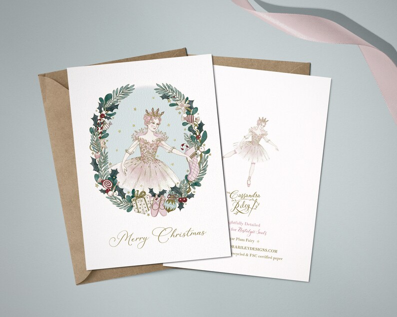 A Christmas card featuring the Sugar Plum Fairy in a pink tutu and a crown, surrounded by a wreath of holly, berries, and ornaments. The text "Merry Christmas" is printed below the ballerina. The back of the card features a smaller image of the ballerina and the artist's name and website.