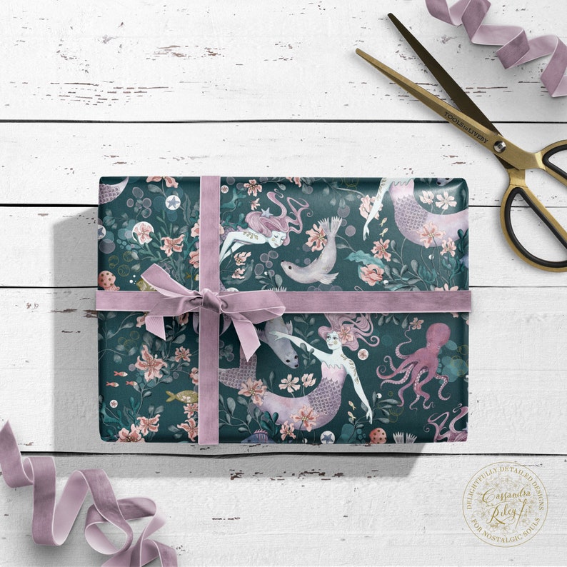 Teal blue gift wrap with a pink ribbon. The wrapping paper features a repeating pattern of mermaids, sea creatures, and flowers. The text "Casandra Riley" is visible in the lower right corner.