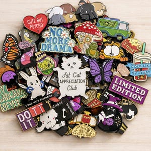 May include: A collection of colorful enamel pins with various designs, including a heart that says "Cute But Psycho", a white cat that says "Fat Cat Appreciation Club", and a purple "Limited Edition" pin. Other pins feature butterflies, mushrooms, and cartoon characters.