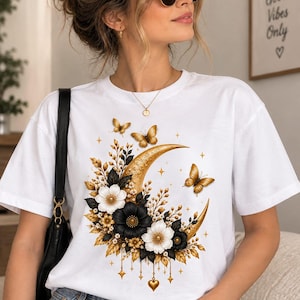Peut inclure: Un t-shirt blanc à manches courtes avec une impression graphique représentant un croissant de lune doré orné de fleurs noires et blanches, de feuillage doré et de papillons. Le motif inclut des petites breloques étoiles et cœurs.