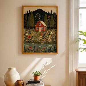 May include: A framed art print depicts a red house nestled in a field of flowers, with a mountain backdrop. The artwork is in a wooden frame and hangs on a cream-colored wall. A wooden cabinet with vases and books is in the foreground.