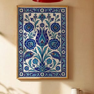 May include: A framed wall art print featuring a detailed floral design in shades of blue and teal on a white background. The artwork is in a gold frame, hanging on a beige wall. A red pendant light hangs above a wooden table.