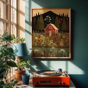 May include: A framed art print depicts a red house nestled in a field of flowers and trees, with a mountain in the background. A vintage orange record player sits on a wooden surface below the artwork, next to a blue lamp and potted plants.