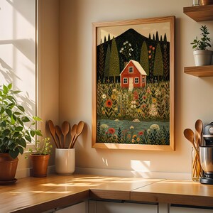 May include: A framed art print depicts a red house nestled in a vibrant meadow with a mountain backdrop. The artwork features a colorful array of flowers, trees, and a flowing river. The print is displayed in a light wooden frame, adding a touch of rustic charm to the scene.