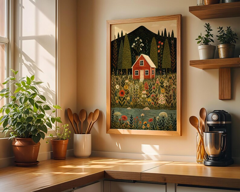 May include: A framed art print depicts a red house nestled in a vibrant meadow with a mountain backdrop. The artwork features a colorful array of flowers, trees, and a flowing river. The print is displayed in a light wooden frame, adding a touch of rustic charm to the scene.
